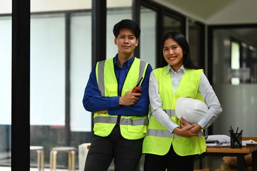 Team of architects wearing reflective jackets with safety helmet in hand standing in office and smiling to camera.