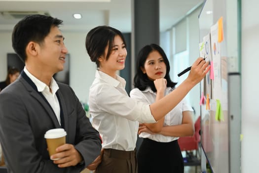 Professional female manager explaining project information on whiteboard during corporate meeting.