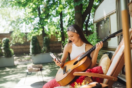 Happy hippie girl are having a good time with playing on guitar in camper trailer. Holiday, vacation, trip concept.High quality photo