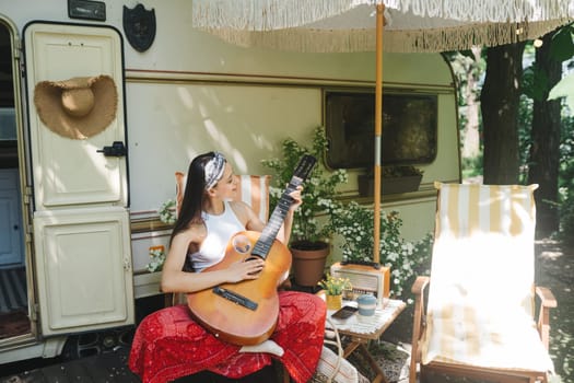 Happy hippie girl are having a good time with playing on guitar in camper trailer. Holiday, vacation, trip concept.High quality photo