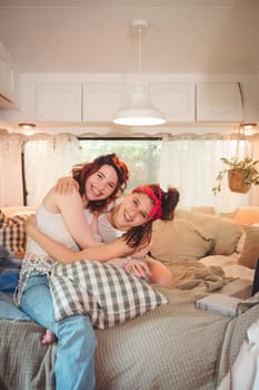 Portrait of a cute lesbian couple. Two girls spend time tenderly together in a camper trailer with LGBT flag on the wall. Love and attitude. LGBT concept. High quality photo