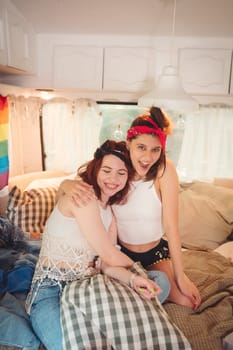 Portrait of a cute lesbian couple. Two girls spend time tenderly together in a camper trailer with LGBT flag on the wall. Love and attitude. LGBT concept. High quality photo