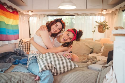 Portrait of a cute lesbian couple. Two girls spend time tenderly together in a camper trailer with LGBT flag on the wall. Love and attitude. LGBT concept. High quality photo