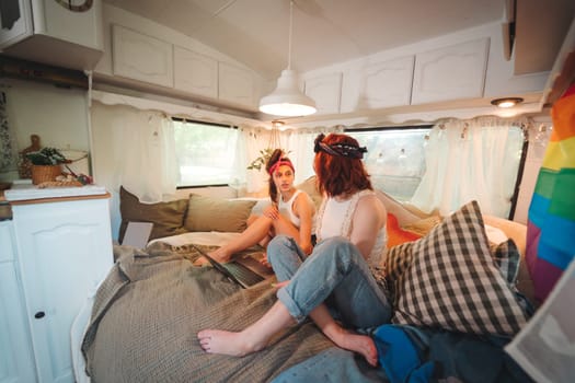 Portrait of a cute lesbian couple. Two girls spend time tenderly together watching movie on laptop in a camper trailer with LGBT flag on the wall. Love and attitude. LGBT concept. High quality photo