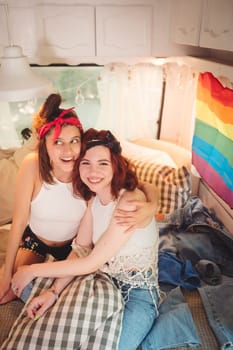 Portrait of a cute lesbian couple. Two girls spend time tenderly together watching movie on laptop in a camper trailer with LGBT flag on the wall. Love and attitude. LGBT concept. High quality photo