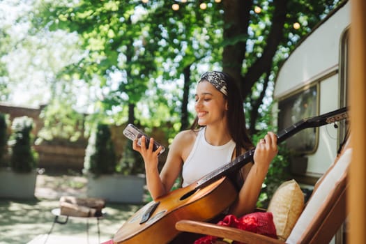 Happy hippie girl are having a good time with playing on guitar in camper trailer. Holiday, vacation, trip concept.High quality photo