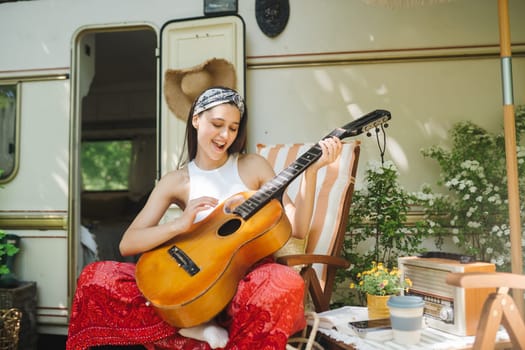 Happy hippie girl are having a good time with playing on guitar in camper trailer. Holiday, vacation, trip concept.High quality photo