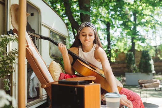 Happy hippie girl are having a good time with playing on guitar in camper trailer. Holiday, vacation, trip concept.High quality photo