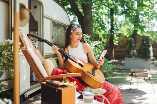 Happy hippie girl are having a good time with playing on guitar in camper trailer. Holiday, vacation, trip concept.High quality photo