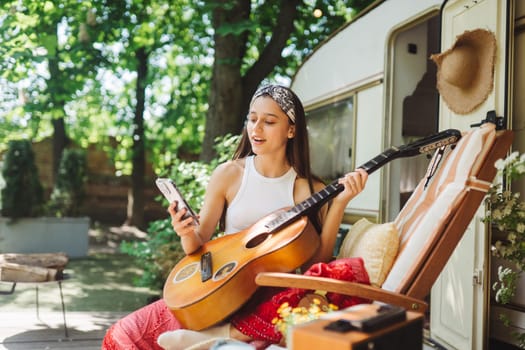 Happy hippie girl are having a good time with playing on guitar in camper trailer. Holiday, vacation, trip concept.High quality photo