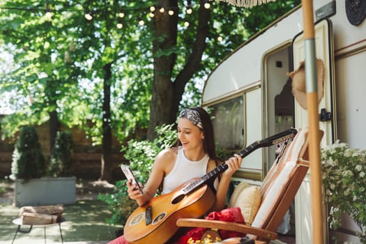 Happy hippie girl are having a good time with playing on guitar in camper trailer. Holiday, vacation, trip concept.High quality photo