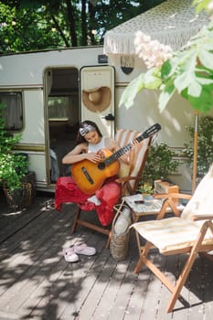 Happy hippie girl are having a good time with playing on guitar in camper trailer. Holiday, vacation, trip concept.High quality photo