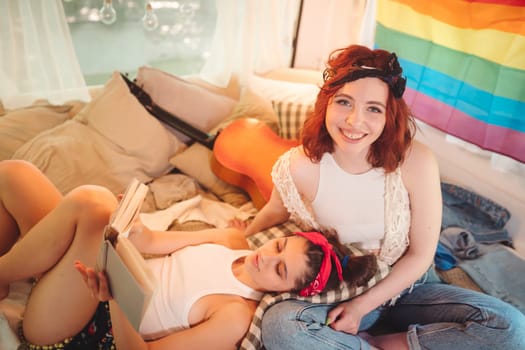 Portrait of a cute lesbian couple. Two girls spend time tenderly together in a camper trailer with LGBT flag on the wall. Love and attitude. LGBT concept. High quality photo