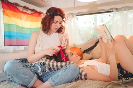 Portrait of a cute lesbian couple. Two girls spend time tenderly together in a camper trailer with LGBT flag on the wall. Love and attitude. LGBT concept. High quality photo