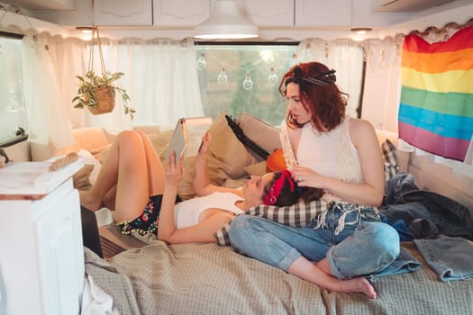 Portrait of a cute lesbian couple. Two girls spend time tenderly together in a camper trailer with LGBT flag on the wall. Love and attitude. LGBT concept. High quality photo