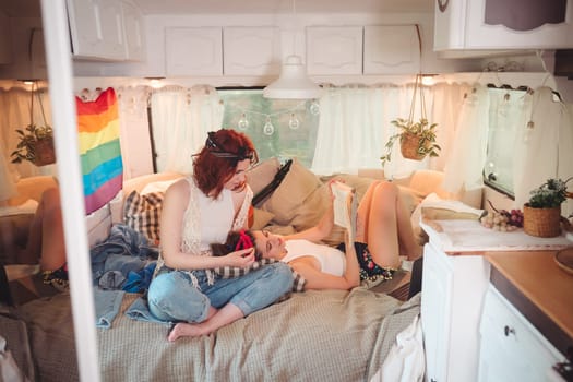 Portrait of a cute lesbian couple. Two girls spend time tenderly together in a camper trailer with LGBT flag on the wall. Love and attitude. LGBT concept. High quality photo