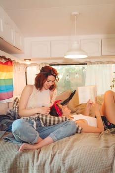 Portrait of a cute lesbian couple. Two girls spend time tenderly together in a camper trailer with LGBT flag on the wall. Love and attitude. LGBT concept. High quality photo