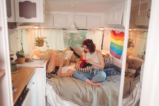 Portrait of a cute lesbian couple. Two girls spend time tenderly together in a camper trailer with LGBT flag on the wall. Love and attitude. LGBT concept. High quality photo