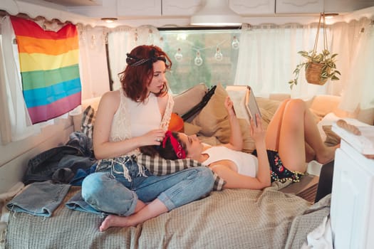 Portrait of a cute lesbian couple. Two girls spend time tenderly together in a camper trailer with LGBT flag on the wall. Love and attitude. LGBT concept. High quality photo