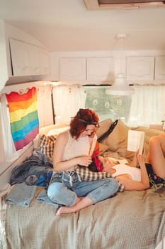 Portrait of a cute lesbian couple. Two girls spend time tenderly together in a camper trailer with LGBT flag on the wall. Love and attitude. LGBT concept. High quality photo