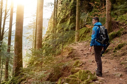 A guy tourist with a backpack stands on a mountain trail and looks into the distance. The concept of travel and adventure. Traveler Man with backpack mountaineering Travel Lifestyle concept mountains on background Summer trip vacations outdoor. Concept of travel and healthy, active lifestyle. Young guy with dreadlocks went hiking in mountains. Man with yellow backpack stands on top of hill and enjoys views of nature.