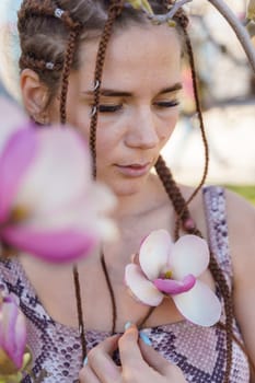 Magnolia flowers. Happy woman enjoys by blooming magnolia tree and sniffs it flowers with closed eyes in spring garden. Portrait