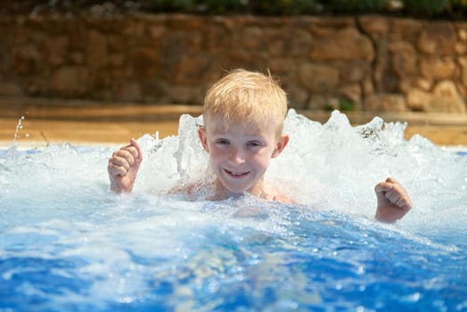 Young boy kid child eight years old splashing in swimming pool having fun leisure activity. Boy happy swimming in a pool. Activities on the pool, children swimming and playing in water, happiness and summertime