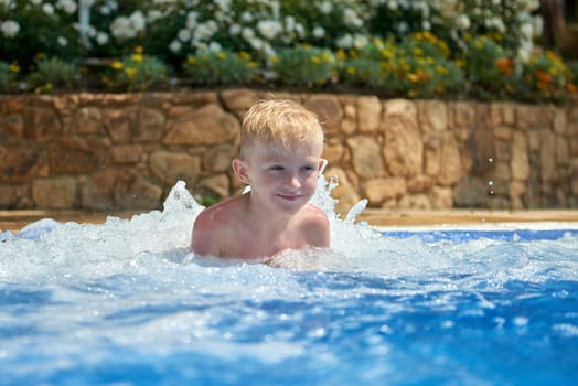 Young boy kid child eight years old splashing in swimming pool having fun leisure activity. Boy happy swimming in a pool. Activities on the pool, children swimming and playing in water, happiness and summertime