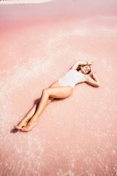 Woman pink salt lake. She lies in a white bathing suit. Wanderlust photo for memory.