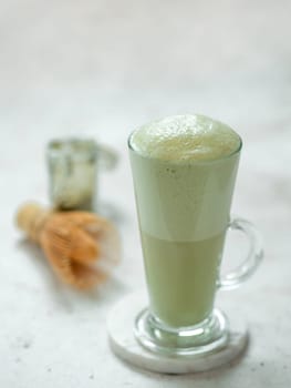 Perfect green matcha tea latte with foam. Matcha green tea latte in glass. Matcha latte on light background. Copy space. Vertical