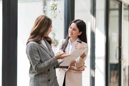 Two happy professional coworkers discussing plan at work. explaining Asian colleague financial project on laptop in office.