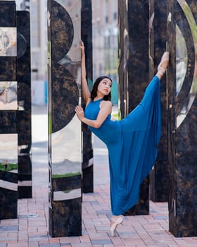 Beautiful asian ballerina in blue dress and pointe shoes posing outdoors