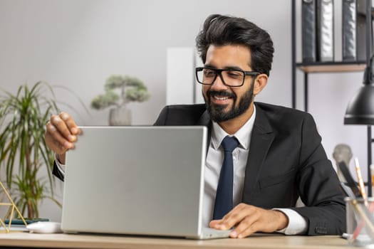 Indian bearded businessman freelancer at home office workplace start working on laptop computer. Professional broker freelancer man opens notebook sends messages makes online purchases watching movies