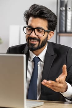 Indian businessman working on laptop computer at home office desk talk on online communication video call with employee, boss. Manager man freelancer support services looking at webcam of computer