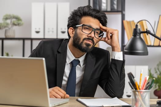 Tired indian businessman feeling worried about financial problem, stress at home office workplace. Indian freelancer broker man frustrated thinking of money debt, budget loss, bankruptcy. Overworking