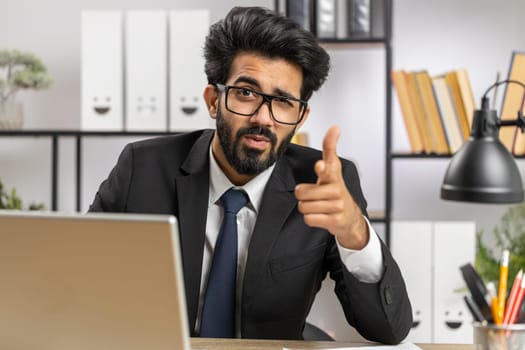 I choose you. Young indian businessman programmer software developer working on office laptop pointing to camera, looking with happy expression, making choice, showing direction. Arab freelancer man