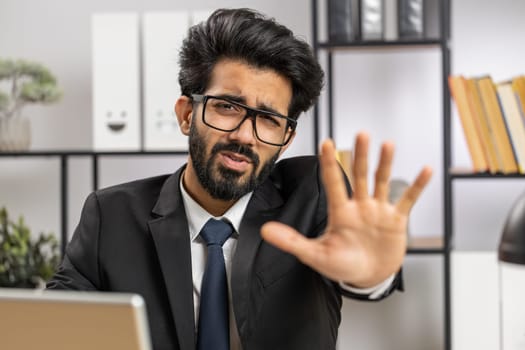 Stop. Indian businessman guy working on laptop, warning of finish, prohibited access, declining communication, body language, rejection, danger trouble. Manager man freelancer at home office workplace