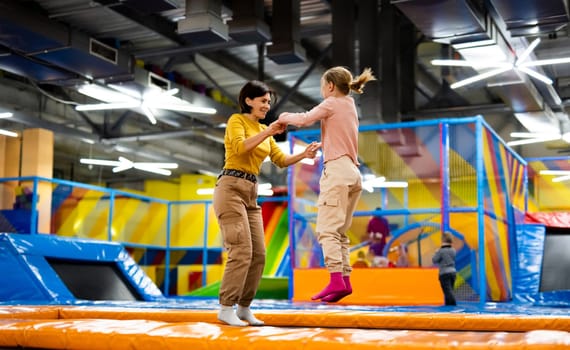 Pretty girl and her daughter kid jumping on colorful trampoline at playground park and smiling. Beautiful family during active entertaiments