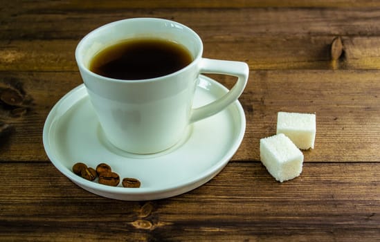 Coffee in a cup, coffee grains and sugar on the table. Coffee in a cup with a saucer, coffee grains and sugar in cubes on a wooden table.