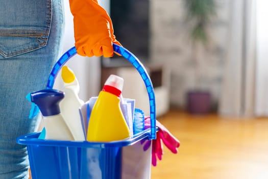 Woman in rubber gloves with bucket of cleaning supplies ready to clean up her apartment. Housewife has many household chores, domestic work and professional cleaning service. Low depth of field