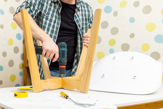 Craftsman collecting and repairing with tools, assembling furniture with drill. Man screws details to chair with electric screwdriver at home after renovation