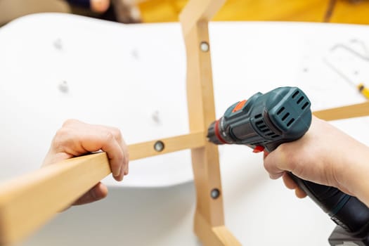 Craftsman collecting and repairing with tools, assembling furniture with drill. Man screws details to chair with electric screwdriver at home after renovation