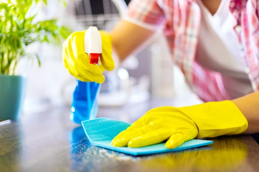 Housewife in yellow gloves wipes dust using spray detergent and rag. The woman is doing household chores. Cleaning concept