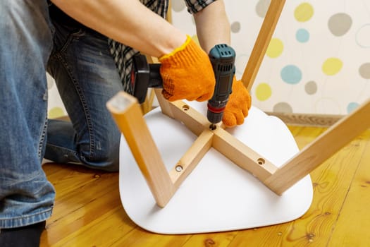 Craftsman collecting and repairing with tools, assembling furniture with drill. Man screws details to chair with electric screwdriver at home after renovation