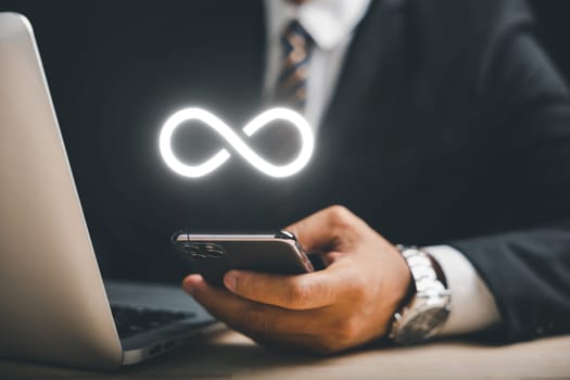 Businessman presents smartphone with infinity symbol, signifying limitless connection in data technology, future unlimited. Infinite power, energy, internet information. technology infinity data