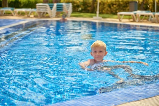 Young boy kid child eight years old splashing in swimming pool having fun leisure activity. Boy happy swimming in a pool. Activities on the pool, children swimming and playing in water, happiness and summertime