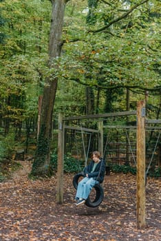 A teenage girl sitting on a swing on the park. Pensive sad child. Thoughtful Sad Teenager Girl Sitting On Playground Roundabout. teenage girl sad on the swing in the park