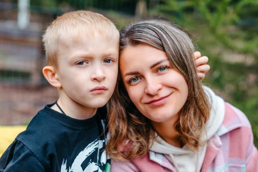 Mother and son outdoor lifestyle portrait in a park setting. Young mother with her seven years old little son are posing. Selective focus. Casual lifestyle photo