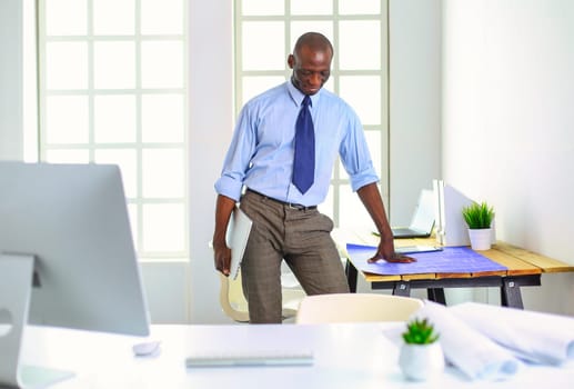 African american architect working with computer and blueprints in office.