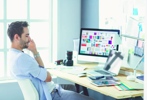 Portrait of young designer sitting at graphic studio in front of laptop and computer while working online